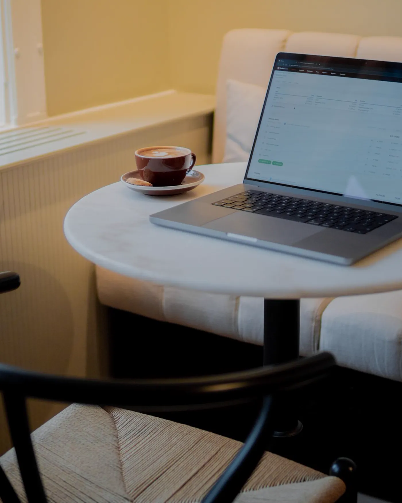 A laptop and notebook open on a wooden table in a warm coffee-shop workspace.